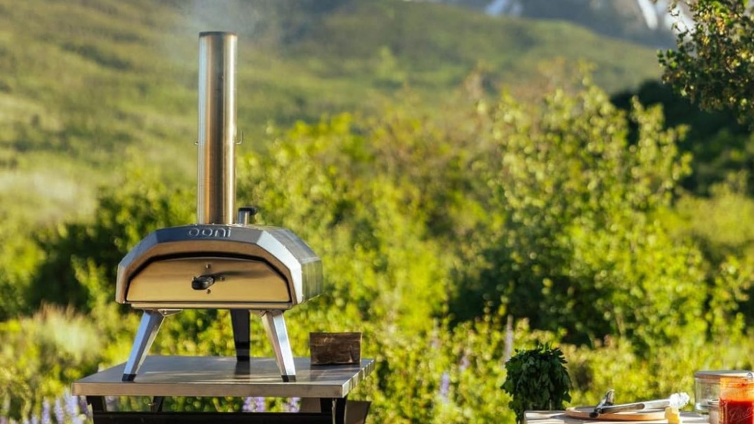 De l’arrière-cour à la maison sur la plage, ce four à pizza portable offre des résultats artisanaux partout – et c’est 100 $ de réduction en ce moment The Ooni Karu 12 pizza oven on a stainless steel table, outside, in front of a mountain
