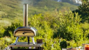 The Ooni Karu 12 pizza oven on a stainless steel table, outside, in front of a mountain
