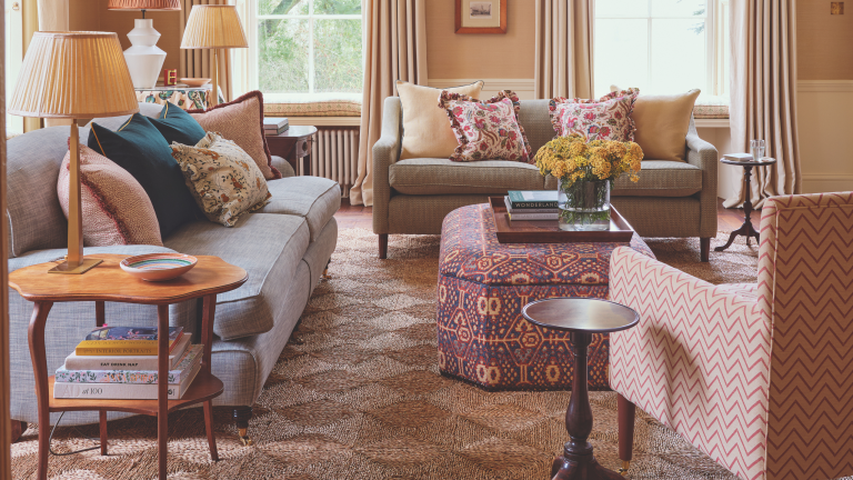 Les poufs sont le secret le moins bien gardé des designers – 20 styles polyvalents qui font des heures supplémentaires dans n’importe quelle pièce The cozy, pattern-filled living room of a 1700s country house restoration by Olivine Design, featuring an upholstered ottoman styled as a coffee table, holding a wooden tray of various objects.