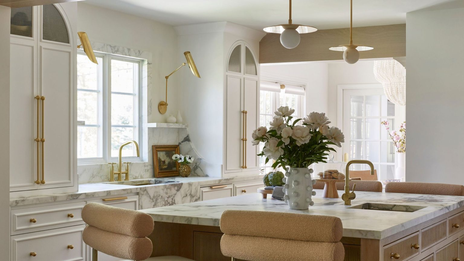 A white kitchen with marble countertops, two sinks, and paneled cabinets