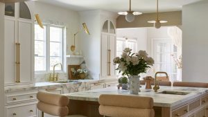 A white kitchen with marble countertops, two sinks, and paneled cabinets