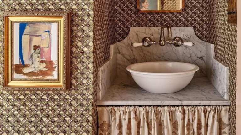 A patterned wallpapered bathroom with a skirted vanity