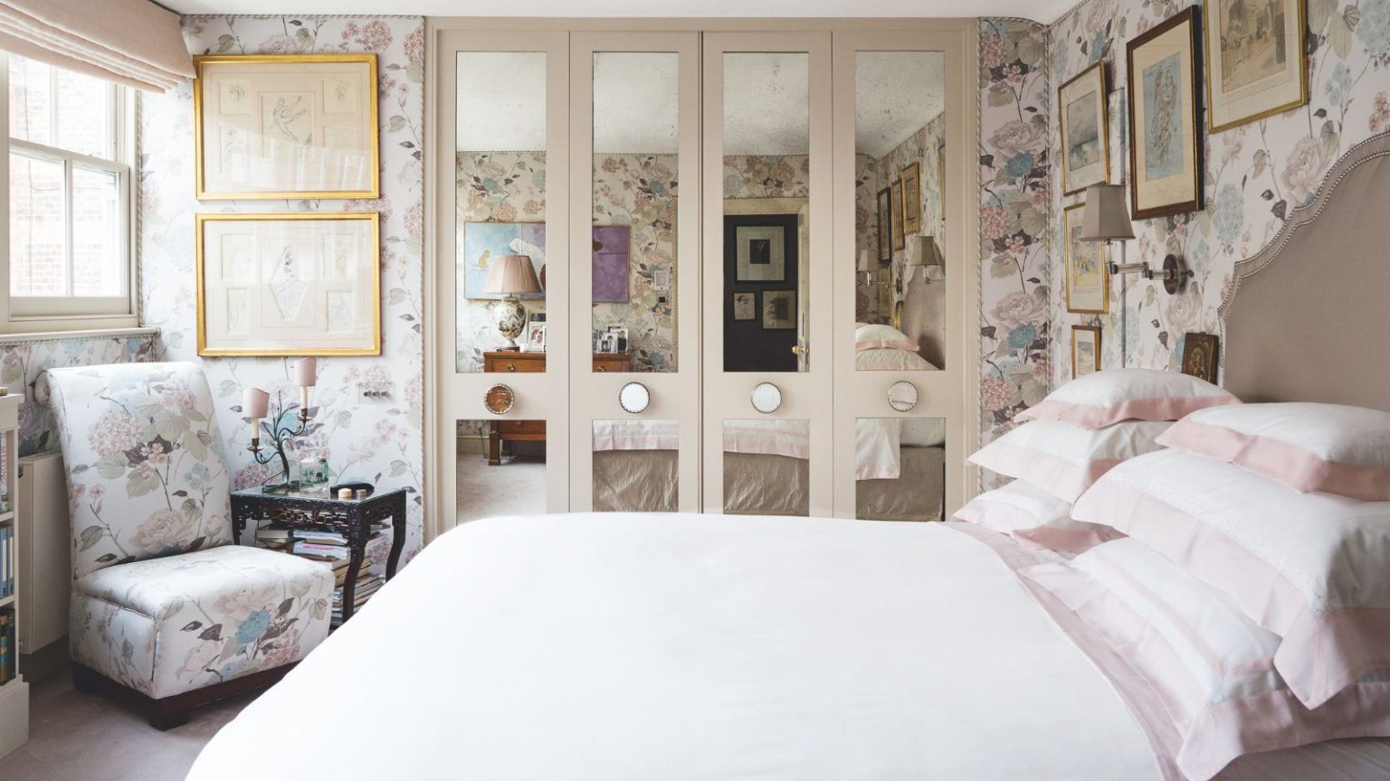 Small bedroom with mirrored four-door built-in closet, white bedding, small chair with side table and floral pastel wallpaper