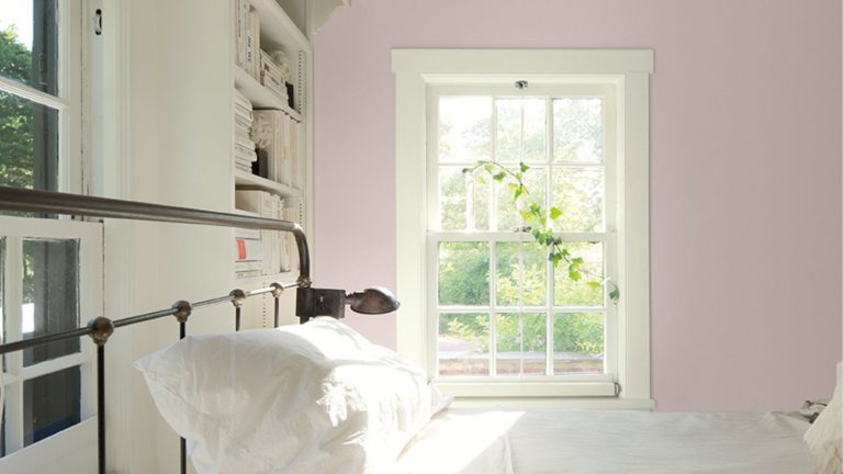 Bedroom with lilac painted walls, black iron bedframe with white linen bedding, and white painted built-in bookshelves and window frame