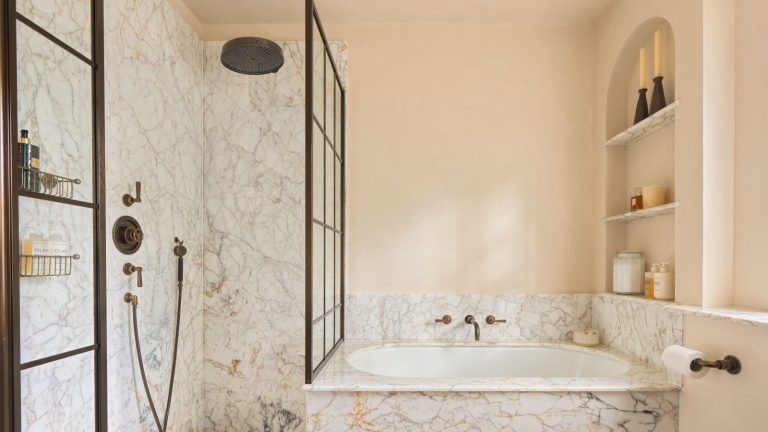 A small bathroom with marble tiles across the bath and shower, a recessed wall niche holding products and glass canisters, and black accent details