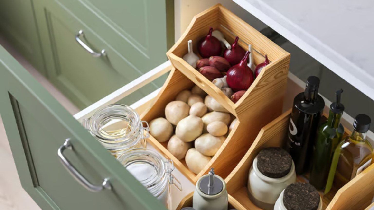 Hero shot of IKEA's stacked wooden food organizers in a deep, open kitchen drawer. It's filled with onions and garlic on top, and potatoes in its lower level.