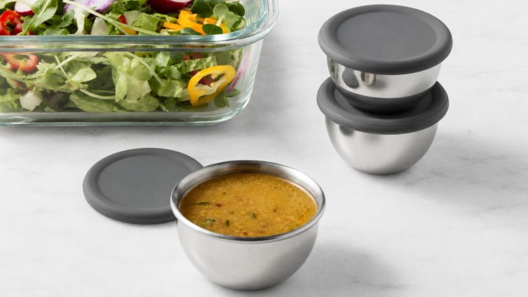 Les chefs professionnels ne jurent que par ces dosettes de préparation alimentaire non toxiques à 7 $ pour rendre la cuisine d’été avec les invités de la maison rapide et facile Three stainless steel condiment containers with grey silicone lids, on a white marble counter beside a glass dish of salad.