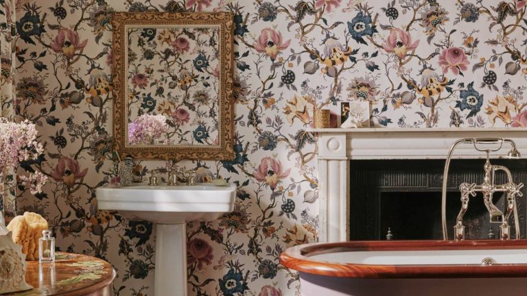 A floral bathroom with a white pedestal sink and an ornate brass mirror