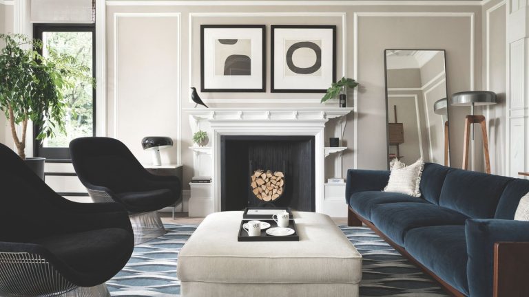Ce sont les 3 couleurs que les designers disent de ne jamais associer avec du gris si vous voulez vraiment qu’il soit beau Living room with pale grey walls, blue velvet sofa, two black armchairs, a pale grey ottoman, a geometric blue rug, a large white fireplace and modern art hanging above it.