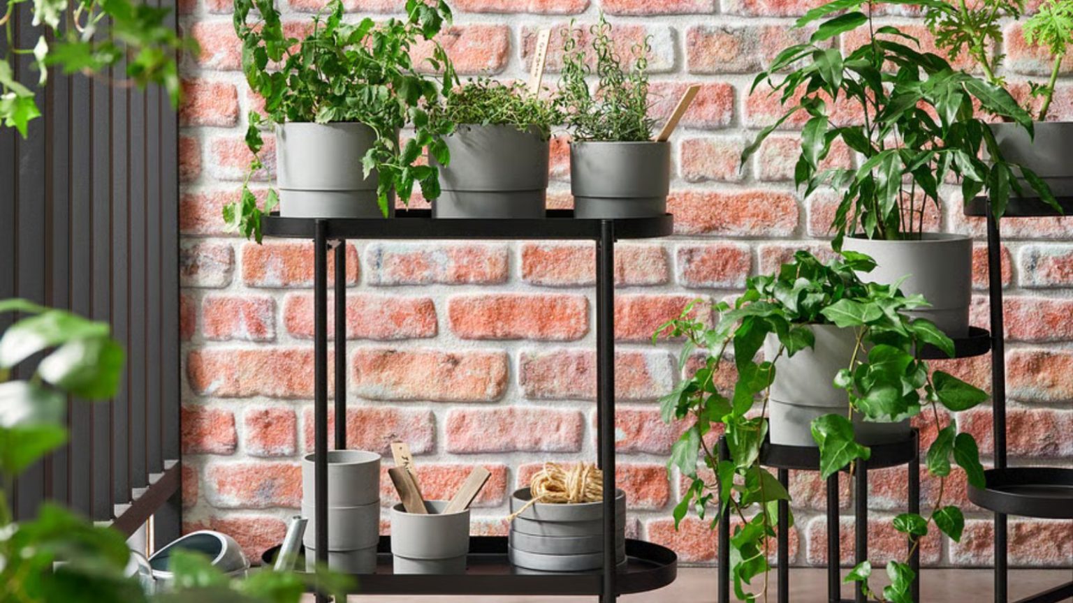 Le support pour plantes élégant d’IKEA est polyvalent, abordable et élégant – si vous recherchez des options de rangement peu encombrantes, il est idéal Black steel plant stand with gray plant pots on a balcony