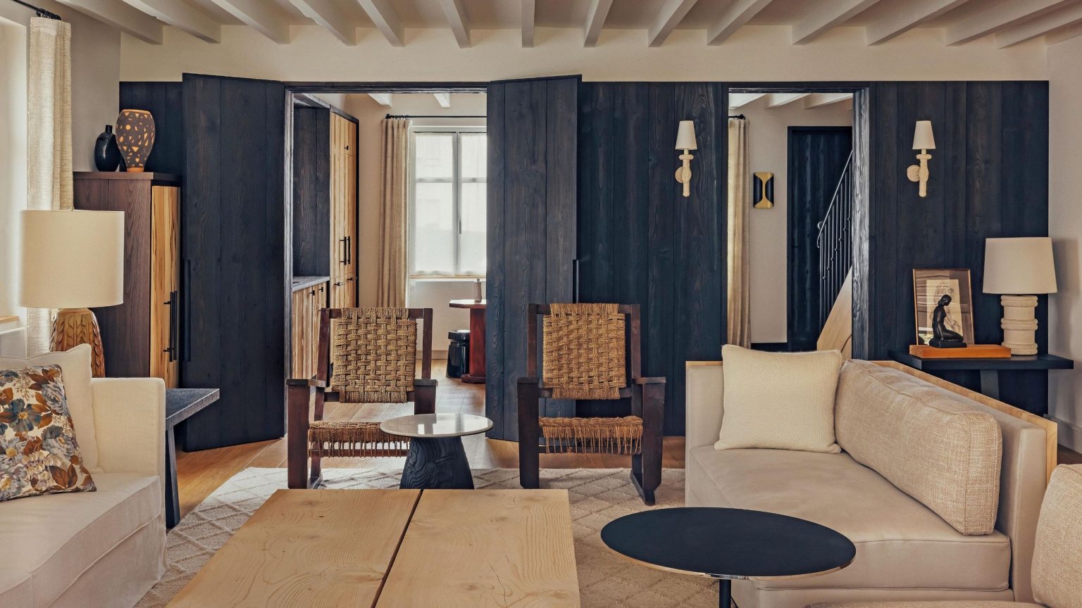 Cette maison de plage française sans prétention cache une retraite pleine d’âme construite autour du cèdre, du contraste et du calme. a rustic living room in a french home with ceiling beams, neutral sofas and navy woodwork