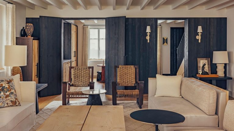 Cette maison de plage française sans prétention cache une retraite pleine d’âme construite autour du cèdre, du contraste et du calme. a rustic living room in a french home with ceiling beams, neutral sofas and navy woodwork