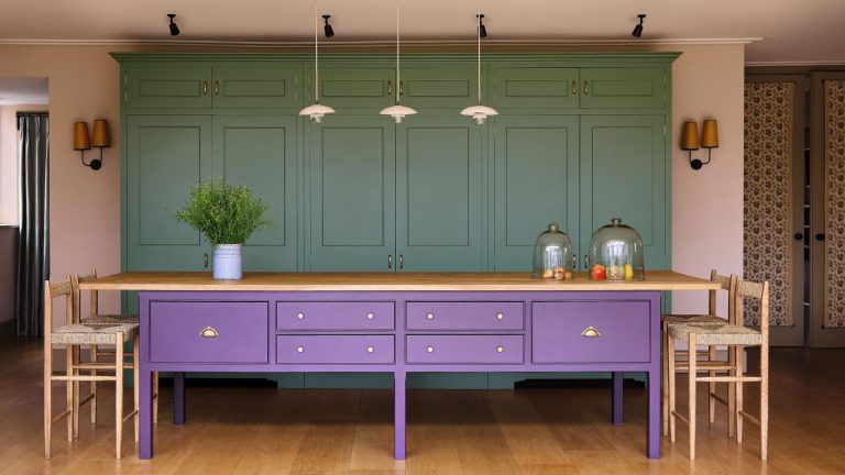 Le bordeaux, le violet et le vert sont des compagnons de lit peu probables – mais la designer Laura Stephens prouve comment ils peuvent fonctionner dans cette maison colorée de Londres a green and kitchen with a large purple island with oak kitchen steels and a trio of pendant lights above