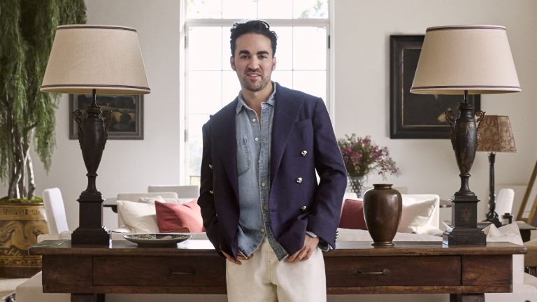 « Les choses ne doivent pas nécessairement être parfaites » – Jake Arnold a appris à adopter le processus pour créer des espaces plus ludiques pour se divertir Jake Arnold standing up and looking to camera waearing a blue blazer and between two lamps