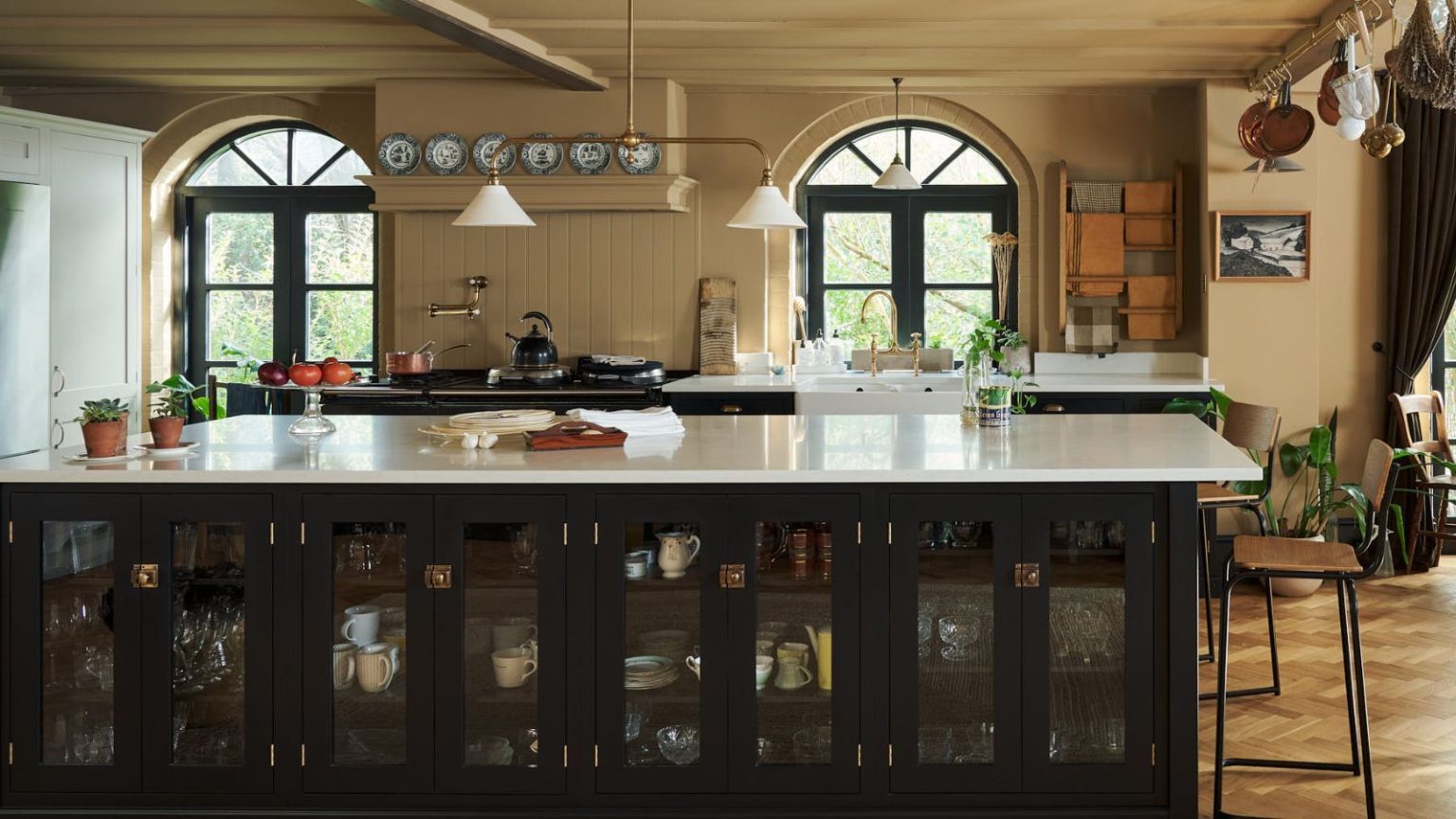 Le seul endroit de cuisine très fréquenté que vous oubliez de nettoyer – et comment le désinfecter sans produits chimiques agressifs Taupe painted kitchen with large black wooden island with a white stone top, and arched windows