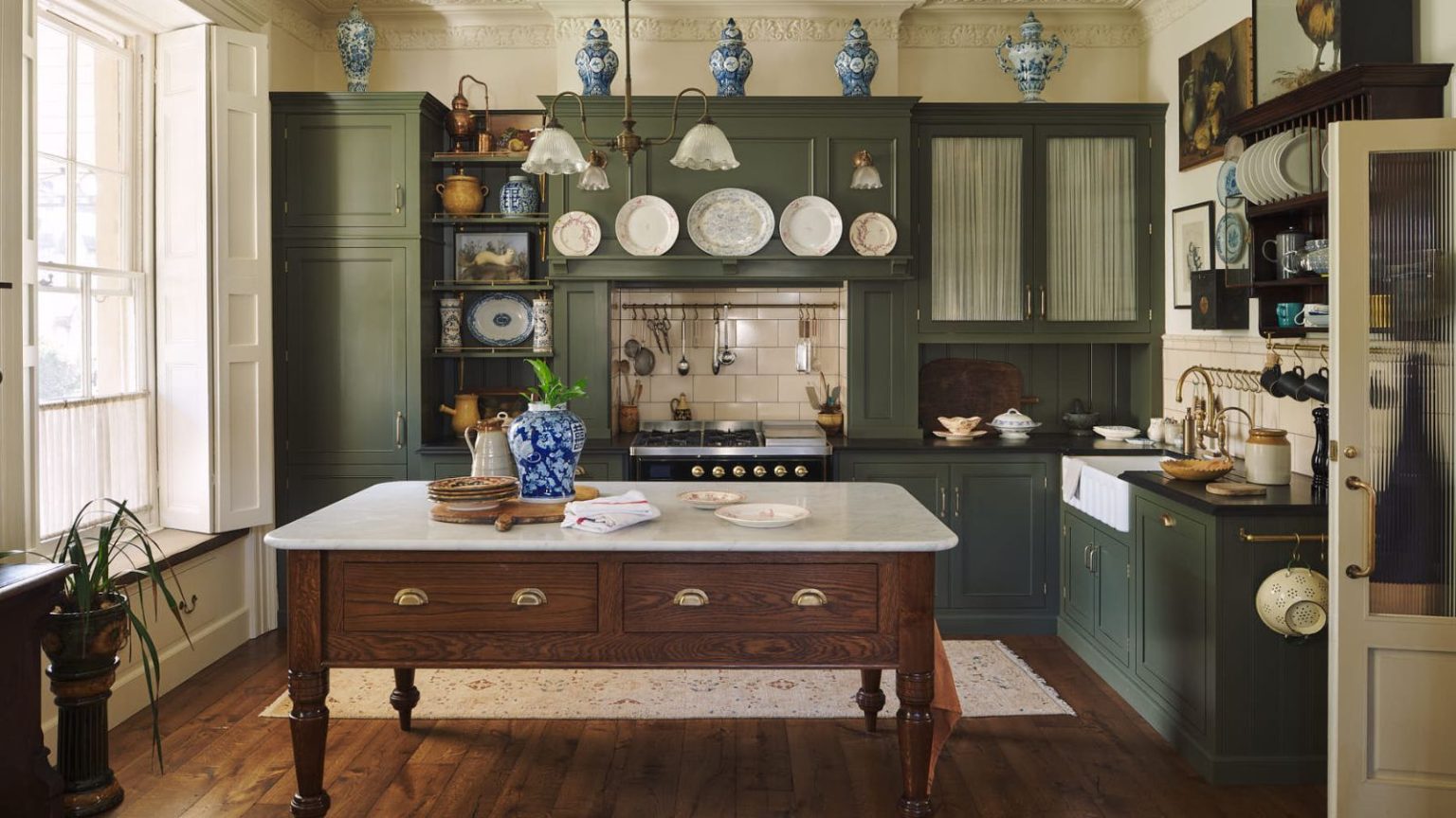 Les pompiers avertissent de ne jamais laisser cet article de cuisine quotidien sur un rebord de fenêtre – et où le stocker en toute sécurité Cream kitchen with tall sunny window to the left, island dining table in the middle, green built-in cabinets and blue porcelain jars decorating the top of cabinets