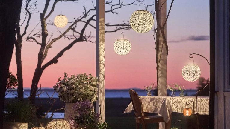 20 lampes solaires extérieures élégantes pour une ambiance estivale sans effort, sans fils en vue Enchanting outdoor patio at sunset featuring a dining table and several etched-metal, Art Nouveau-inspired solar lights