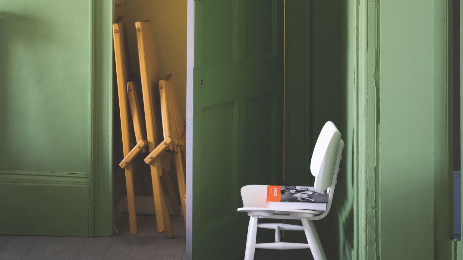 Chartreuse-painted storage room featuring folded furniture and a white mid-century-style chair