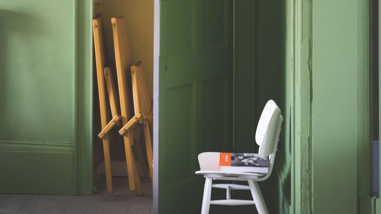 Chartreuse-painted storage room featuring folded furniture and a white mid-century-style chair