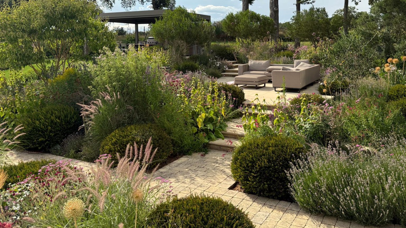 L’approche de plantation en couches qui, selon les concepteurs, rendra votre jardin cher d’ici l’été split level garden design featuring planting beds, raised patio area with garden furniture and pergola, all linked by brick paths