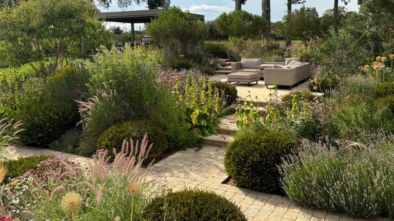 split level garden design featuring planting beds, raised patio area with garden furniture and pergola, all linked by brick paths