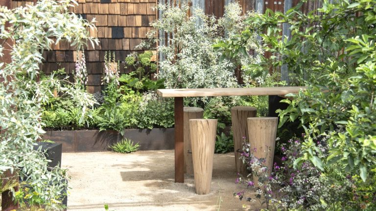 Cette erreur de jardinage facile à commettre en juin pourrait empêcher votre jardin de prospérer – voici ce qu’il faut faire à la place A wooden table and chairs surrounded by raised beds with green shrubs at the RHS Chelsea Flower Show 2026