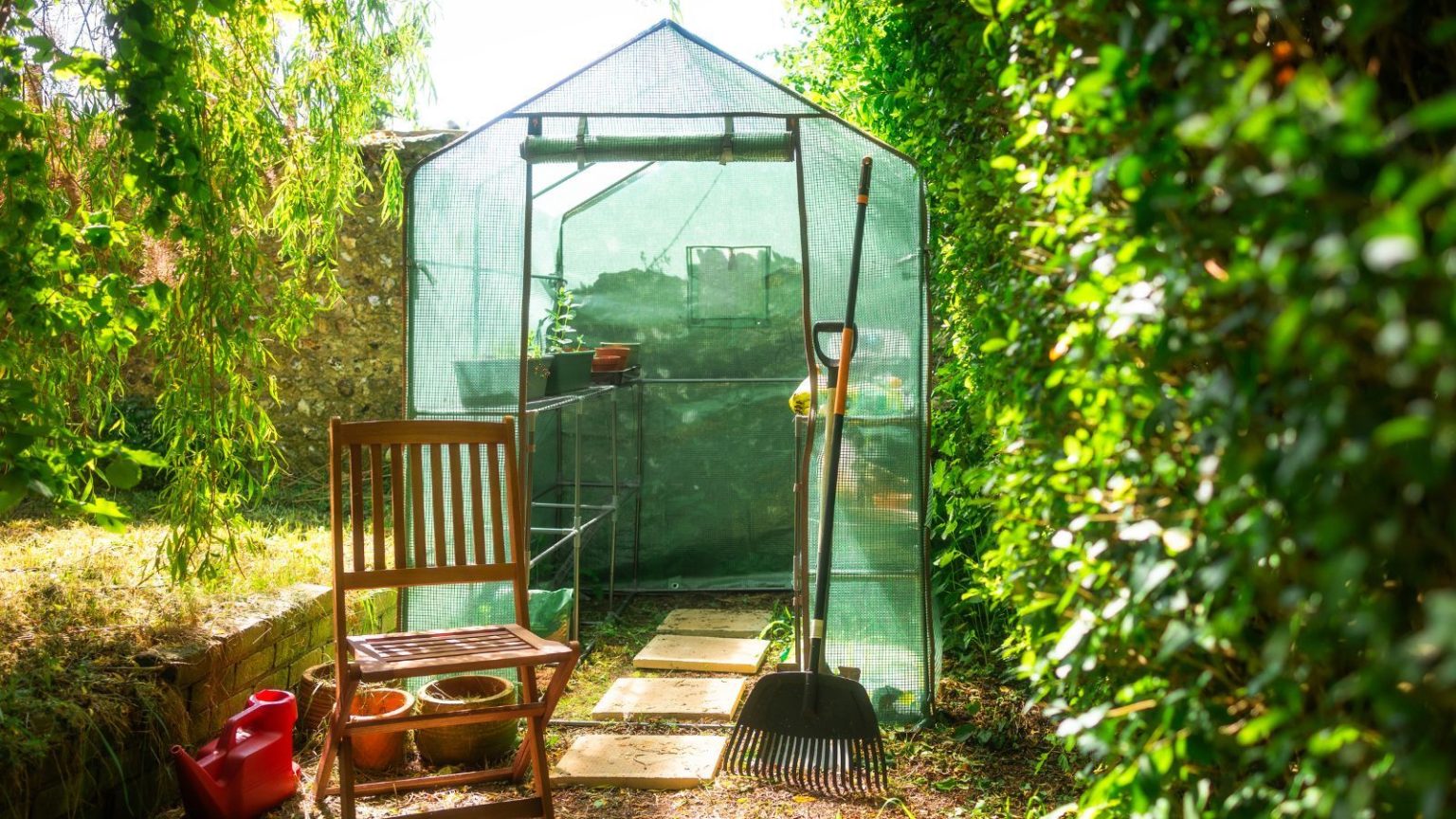 Cette mini serre change la donne dans le petit jardin – vous aidant à cultiver plus de nourriture, de fleurs et d’herbes dans un petit espace Green mesh greenhouse next to wooden chair and rake