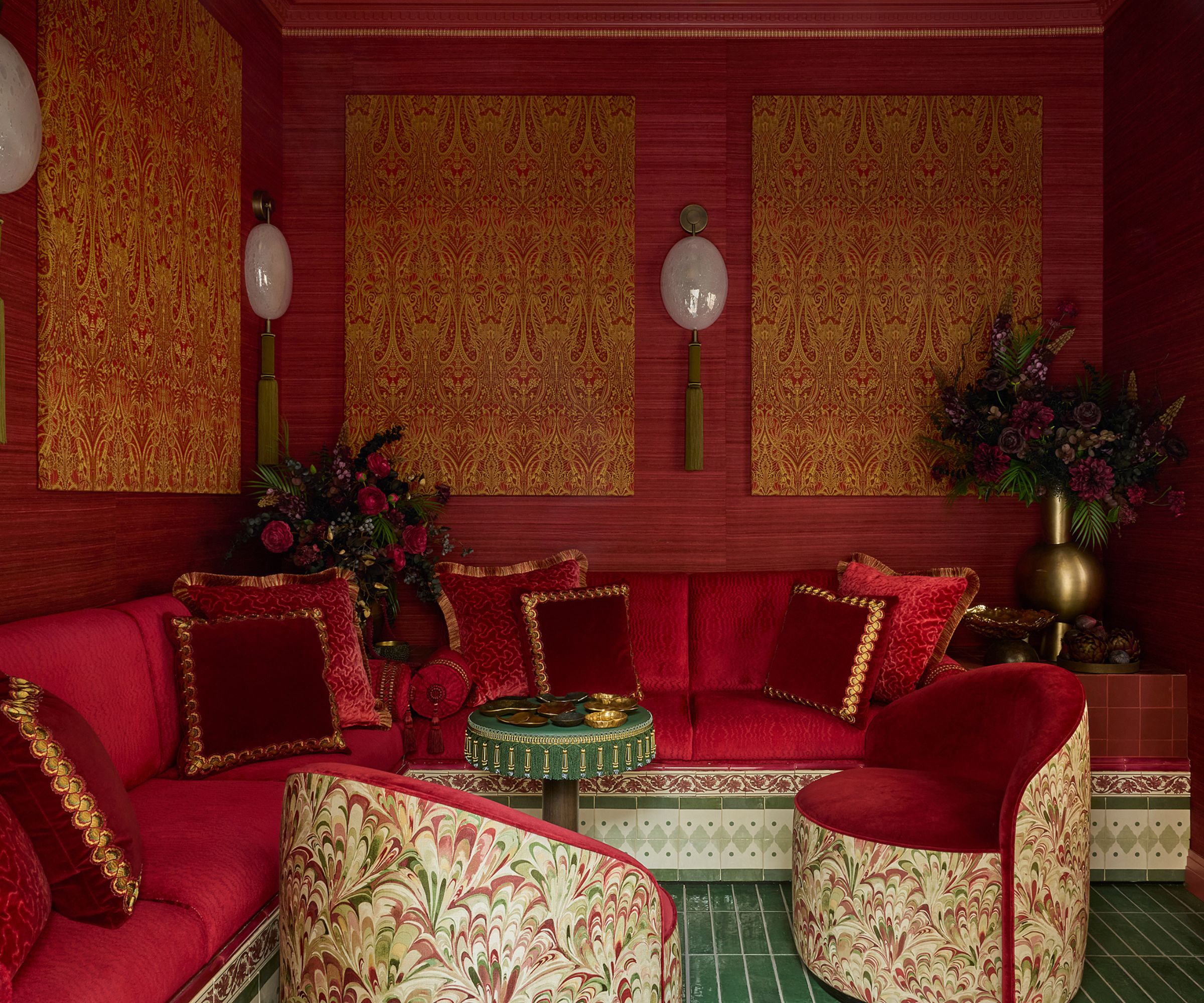 un salon de jardin recouvert de tissu rouge et de tissu avec une banquette carrelée, un sol carrelé vert et de petits fauteuils pour WOW!House 2026