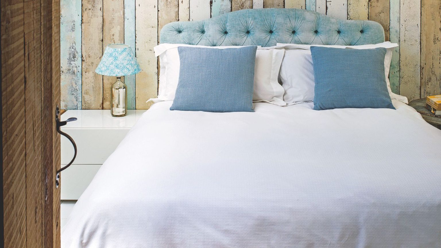 Double panelled bedroom with blue headboard, white bedding, blue cushions, white nightstand and gold lamp with blue and white patterned lampshade