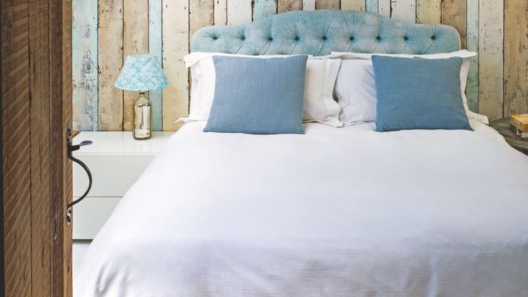 Des experts en CVC révèlent la raison cachée pour laquelle votre chambre est plus chaude – et la solution en 30 secondes pour la refroidir rapidement Double panelled bedroom with blue headboard, white bedding, blue cushions, white nightstand and gold lamp with blue and white patterned lampshade