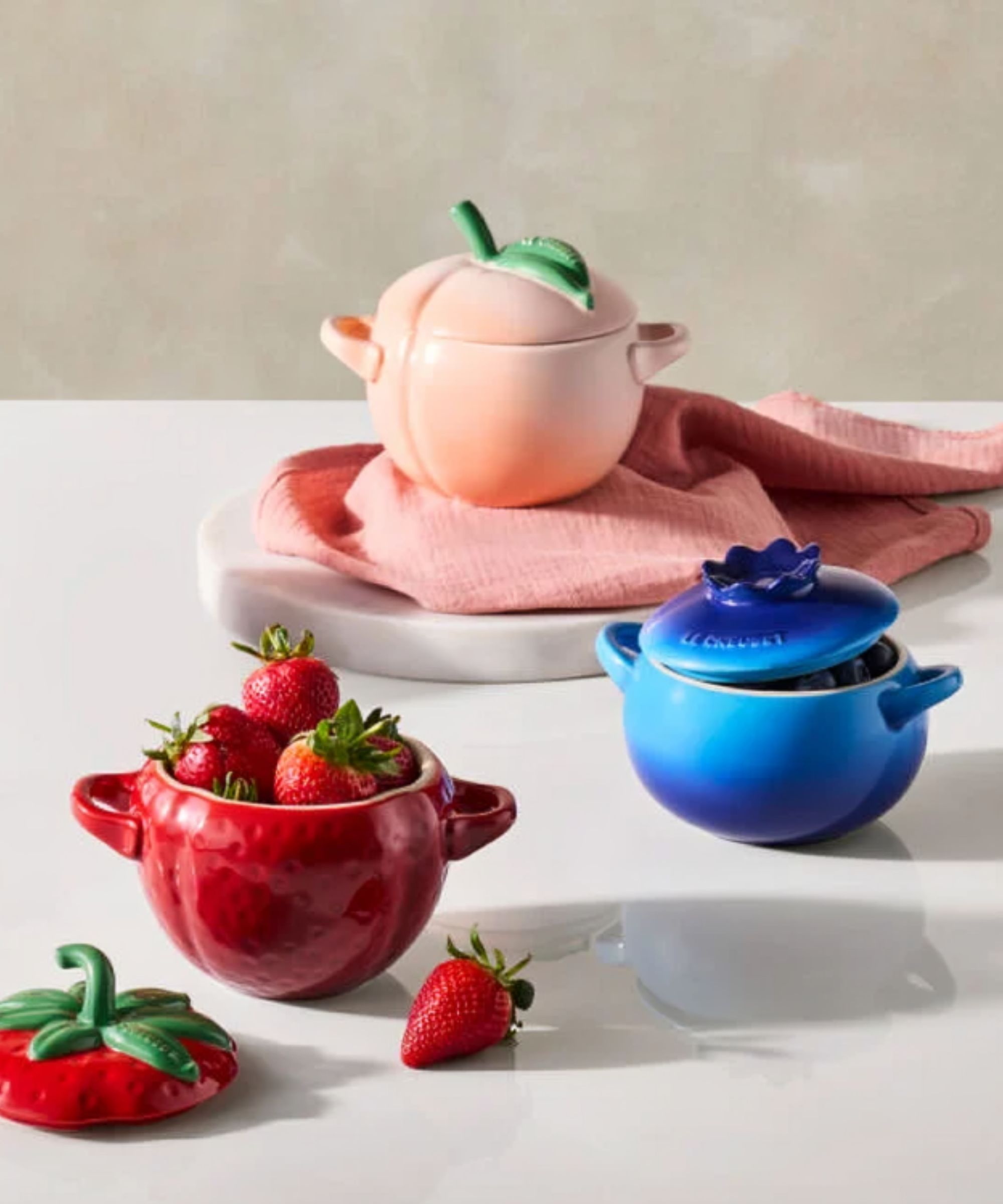 Un ensemble de trois cocottes en forme de fruit, dans un design pêche, fraise et myrtille