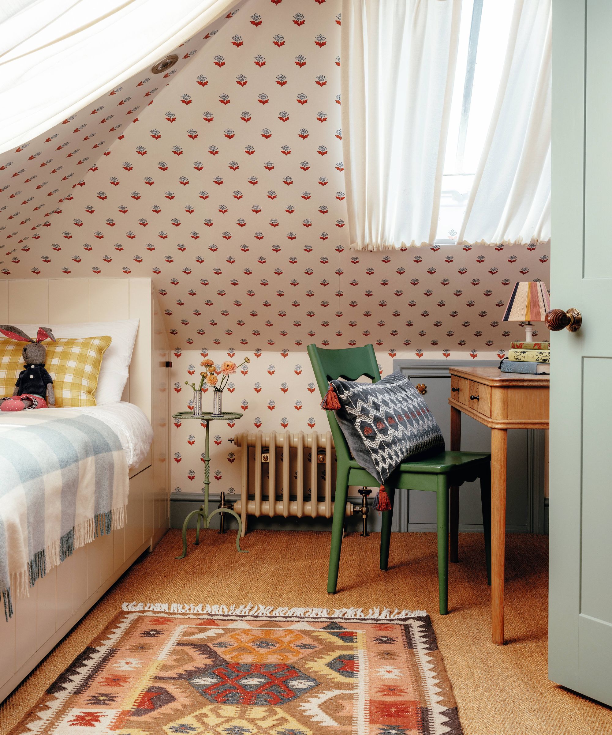 une chambre d'enfant mansardée avec des murs et un plafond recouverts de papier peint floral, des boiseries peintes en vert, un lit simple intégré et un petit bureau en bois avec une chaise verte