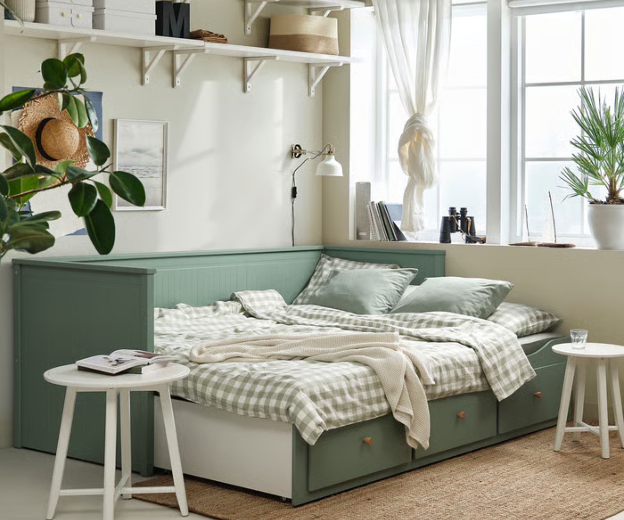 Lit IKEA HEMNES vert sauge avec literie en vichy, avec un tapis en jute, des tables d'appoint en bois blanc et des étagères blanches au-dessus avec des paniers et des boîtes de rangement.