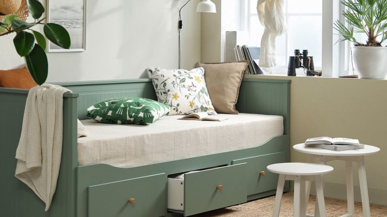 Le lit 3-en-1 le plus vendu d’IKEA vient de bénéficier d’un rafraîchissement chic – apportant l’une des plus grandes tendances de couleurs de 2026 aux petits espaces IKEA grey green HEMNES bed in a living room with floral cushions, large white windows, a pair of white round tables and a jute rug.