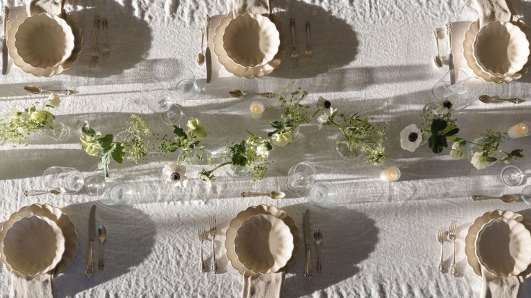 5 erreurs qui donnent à votre table extérieure un aspect bon marché – évitez-les cet été avec ces solutions faciles Outdoor tablescape with white linen tablescape, cream scalloped plates and bowls, a floral garland in the centre, and lit candles