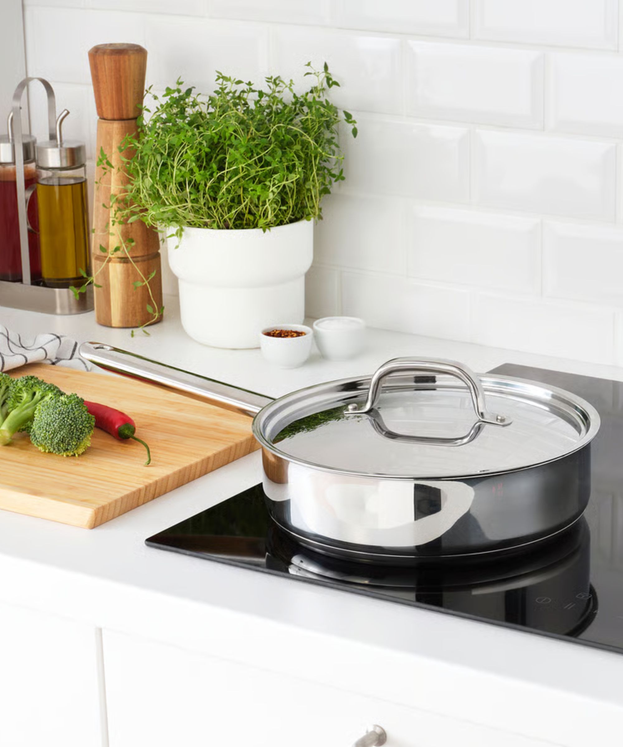 Un saut&eacute; poêle avec un long manche et un couvercle assorti sur une cuisinière électrique noire.