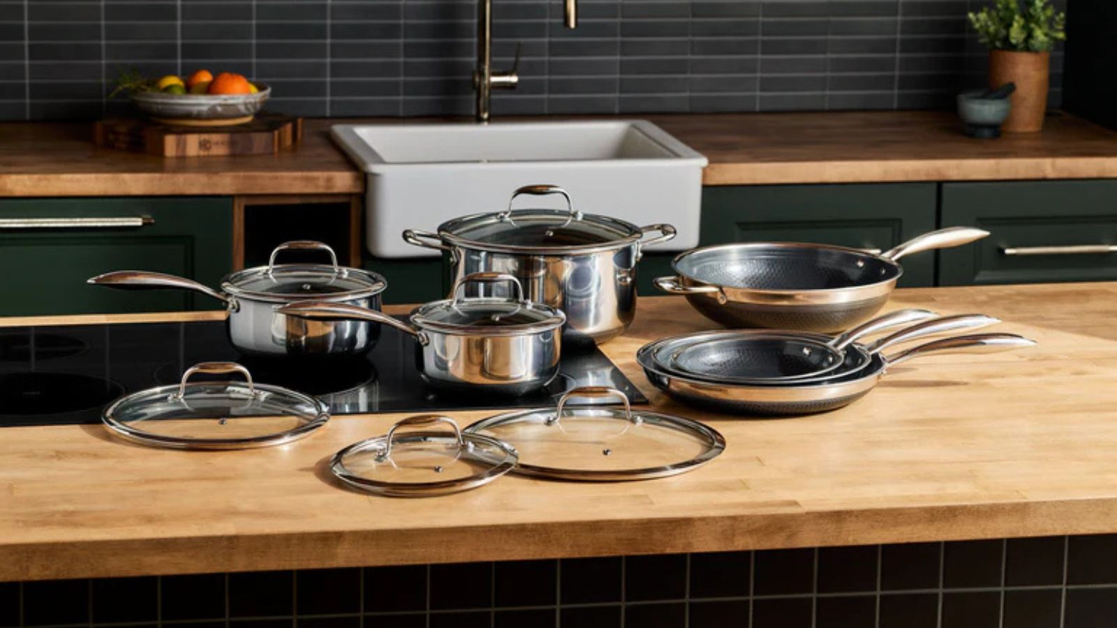 Un ensemble complet de poêles Hexclad hyrid en acier inoxydable sur un comptoir de cuisine en bois avec une cuisinière noire installée à l'intérieur. 