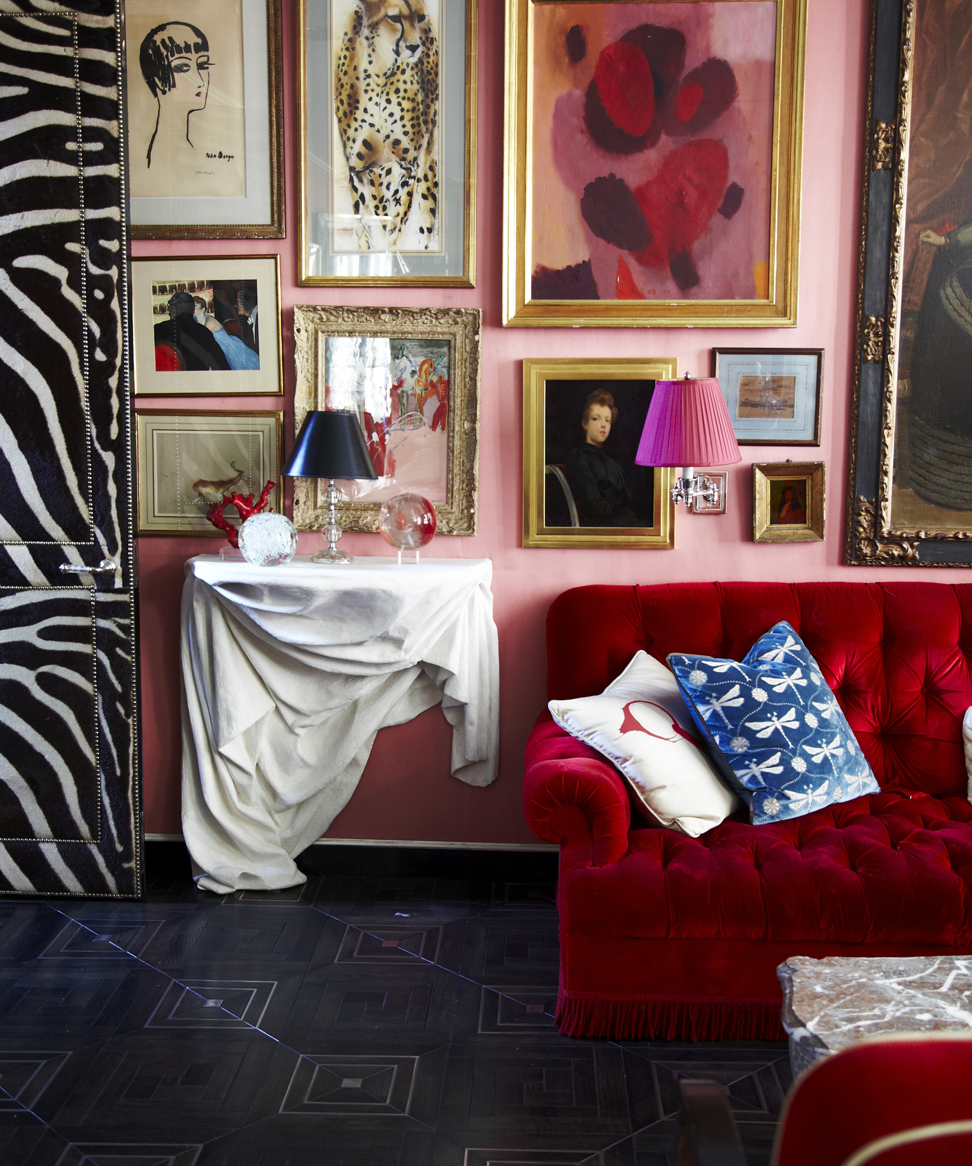 Salon maximaliste avec mur rose, canapé rouge et beaucoup d'œuvres d'art accrochées au mur