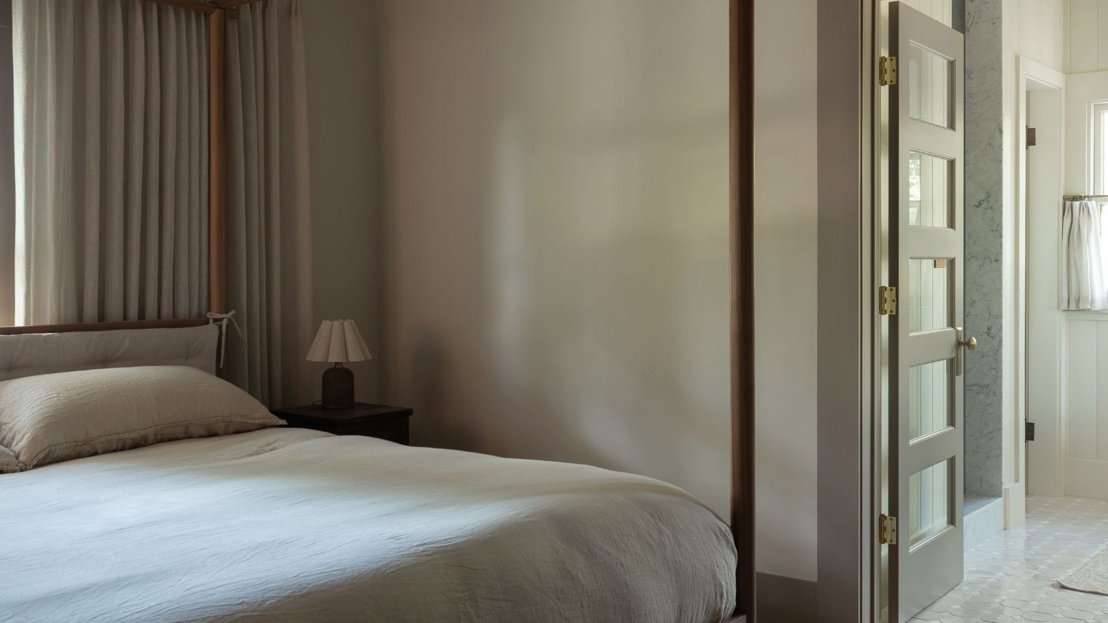 Une chambre moderne et apaisante avec des murs taupe et des moulures en forme de champignon sombre, un lit à baldaquin minimaliste avec une literie crème croustillante et des rideaux neutres. 