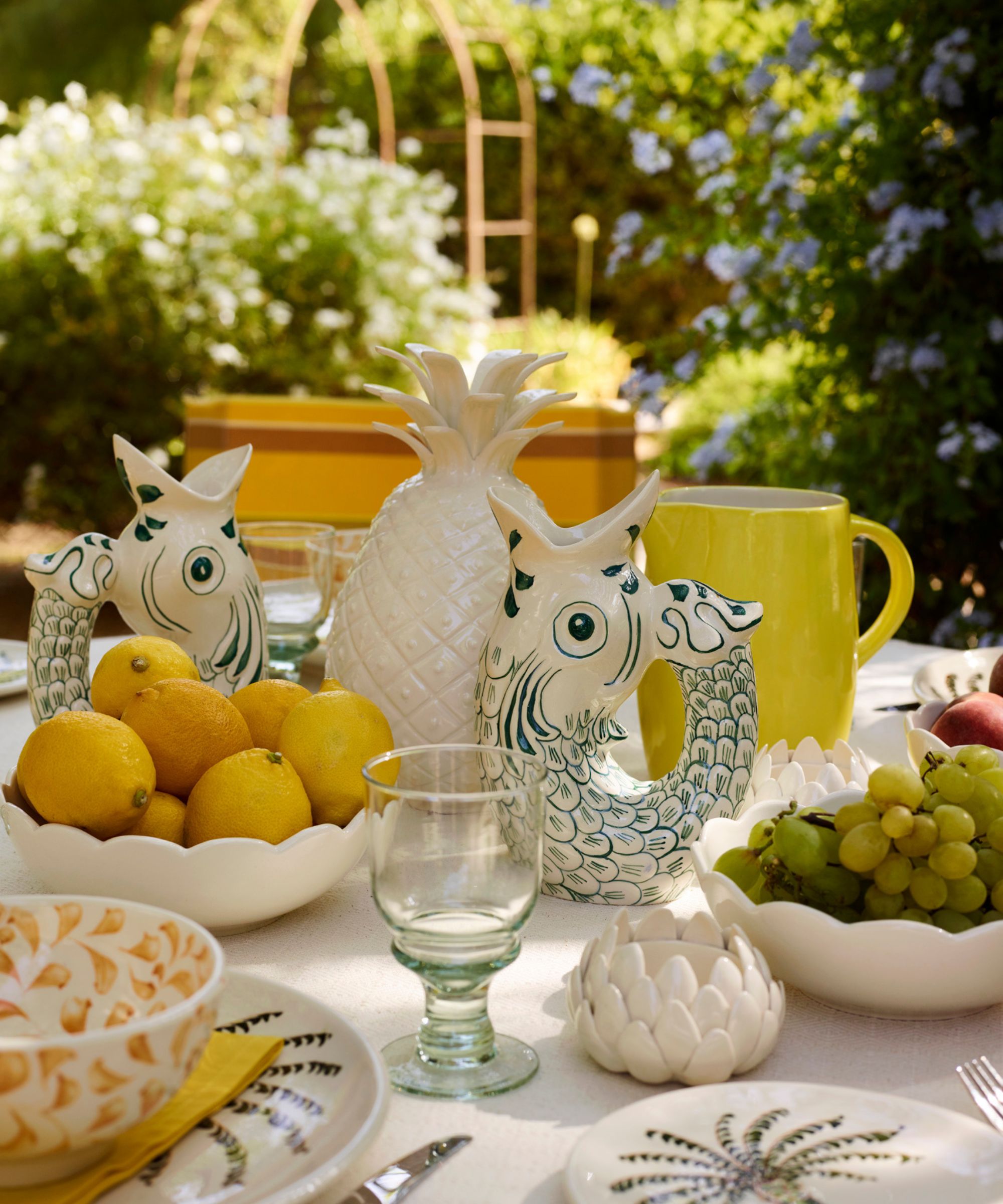 Table de dîner en plein air sur le thème méditerranéen avec cruches à poisson, pièce maîtresse en forme d'ananas, bol de citrons et assiettes en palmier