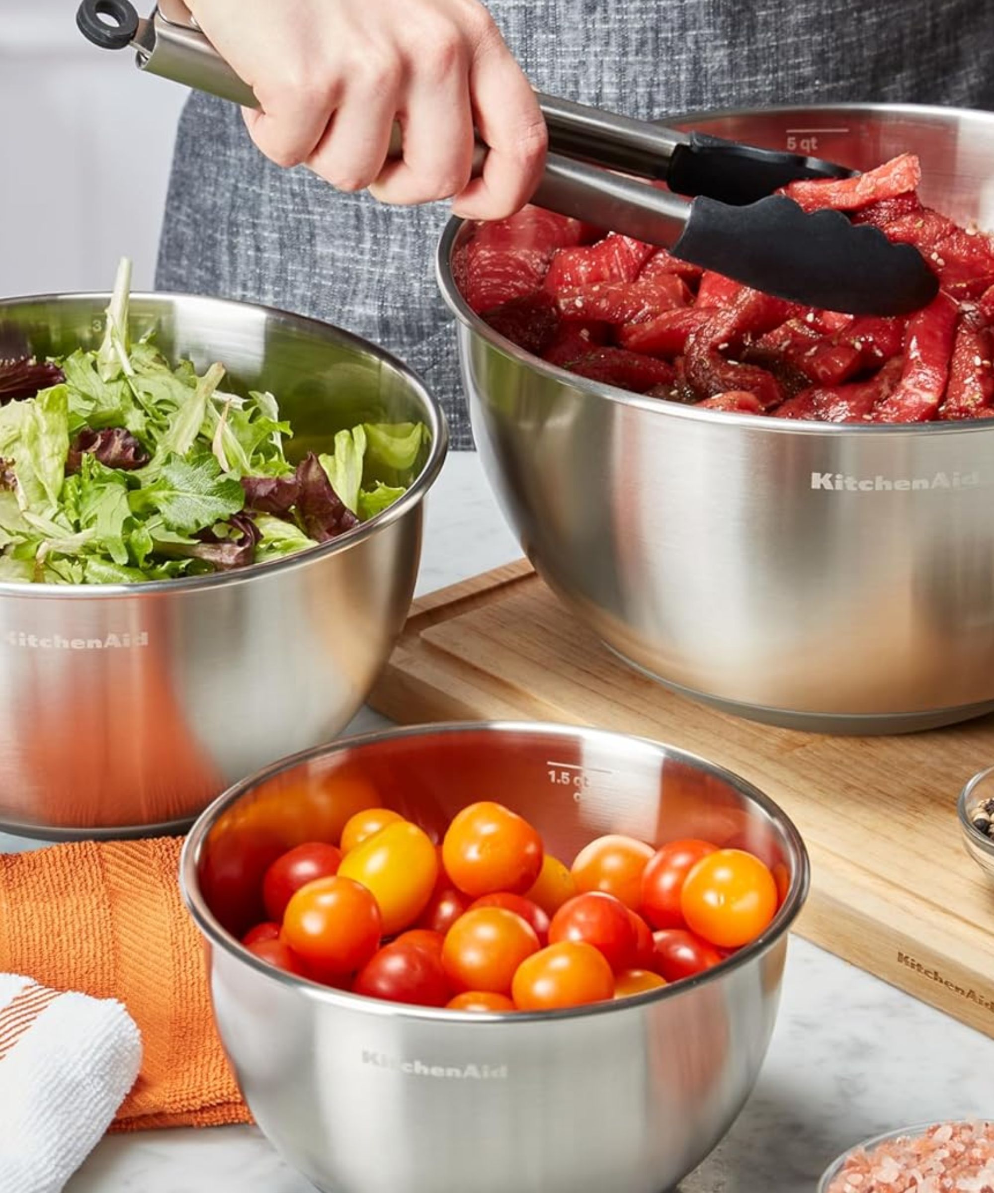Un ensemble de trois bols à mélanger KitchenAid en acier inoxydable utilisés dans une cuisine utilisée pour préparer de la viande et des légumes