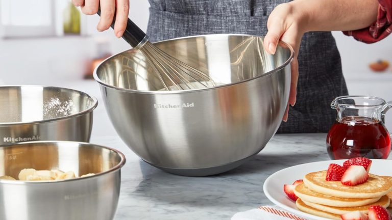 A set of three stainless steel KitchenAid mixing bowls being used in a kitchen to mix cake batter