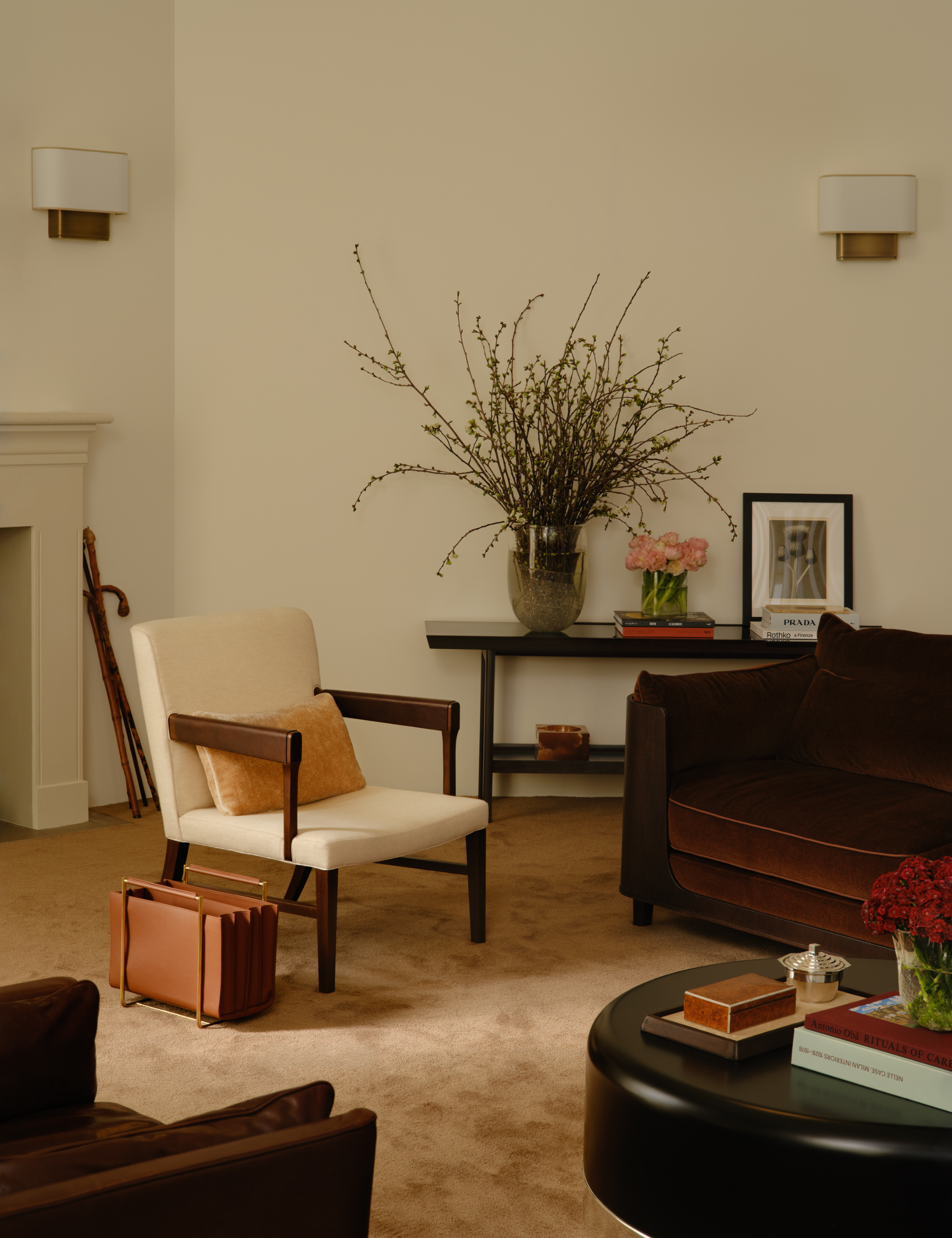 Salon neutre comprenant un porte-revues en cuir, une table basse ronde laquée, une chaise d'appoint inspirée du milieu du siècle et un canapé chocolat surbaissé.