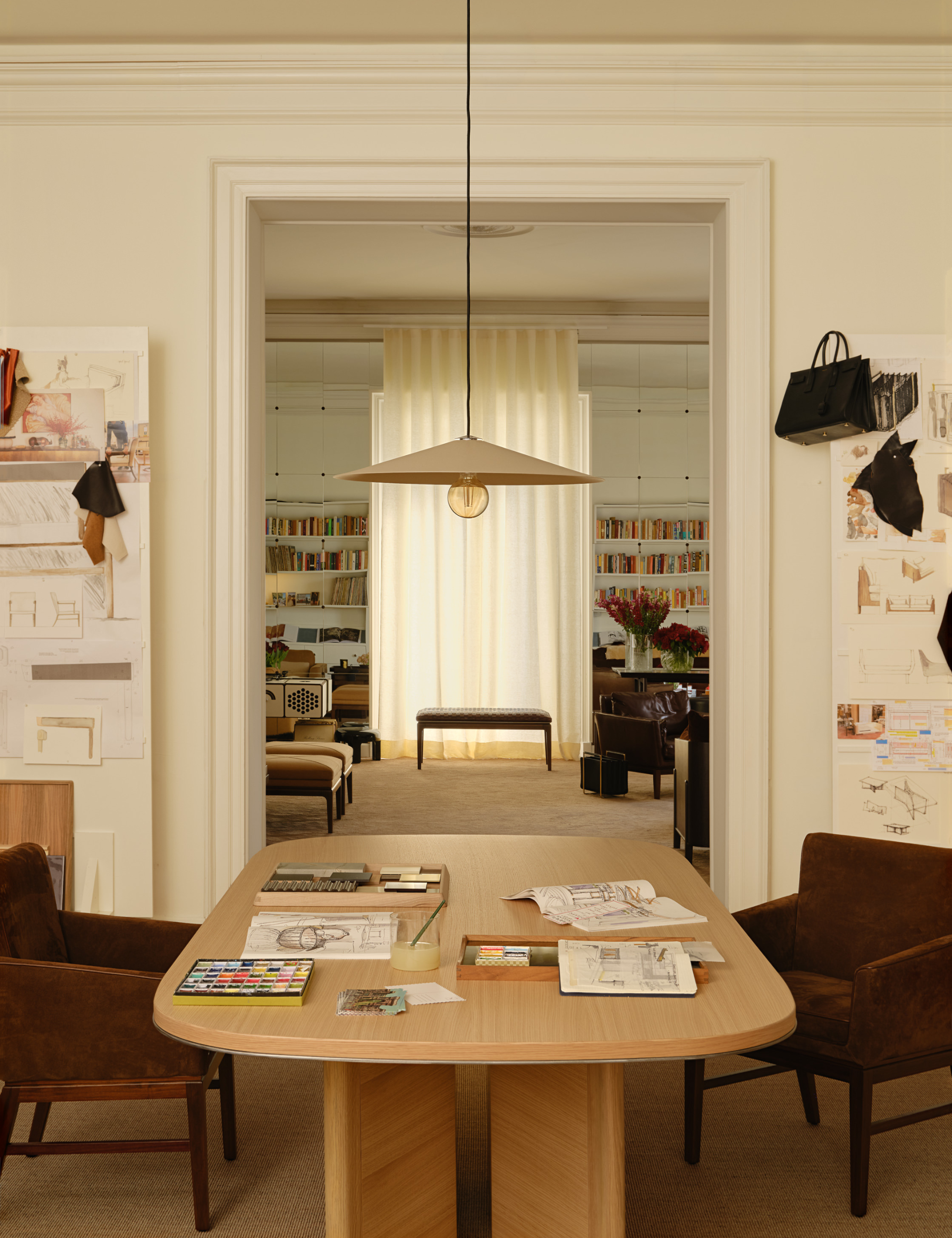 Salle à manger éclectique remplie d'œuvres d'art mettant en valeur la création de GACHOT par Artemest avec des croquis et des échantillons collés aux murs et étalés sur la majestueuse table à manger en bois de chêne.