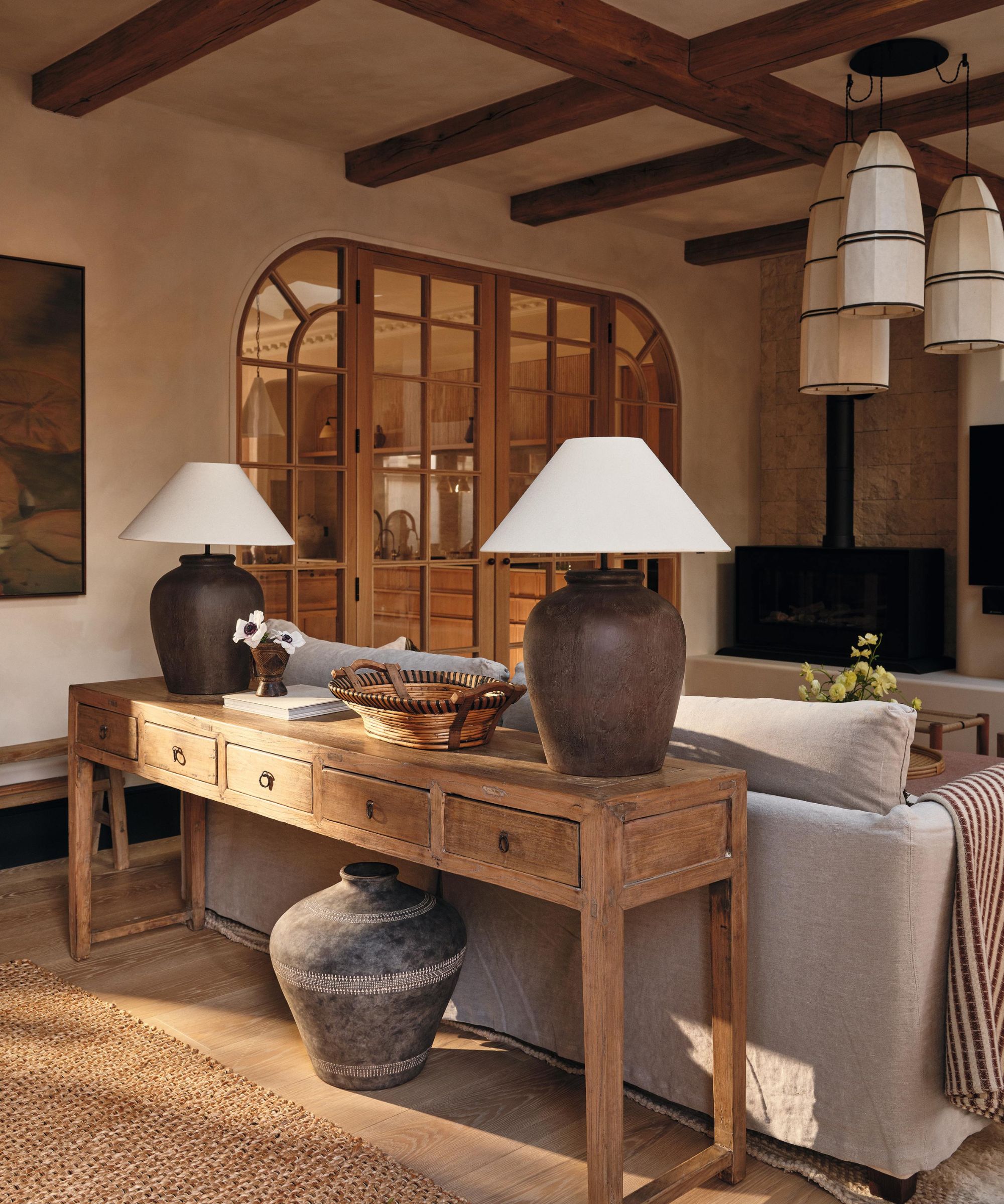 un grand salon d'extension blanchi à la chaux avec des portes cintrées en chêne et en verre, des poutres au plafond et une console en bois rustique