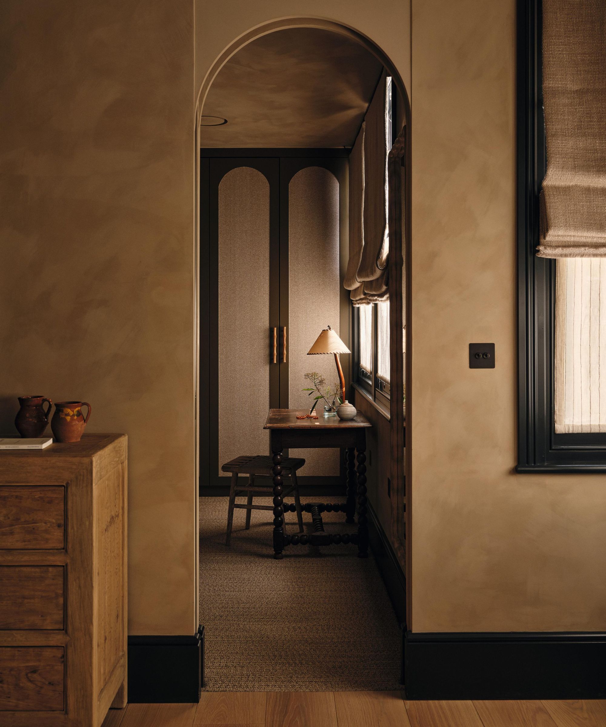une chambre beige à la chaux avec des boiseries peintes en noir et une porte cintrée menant à un dressing