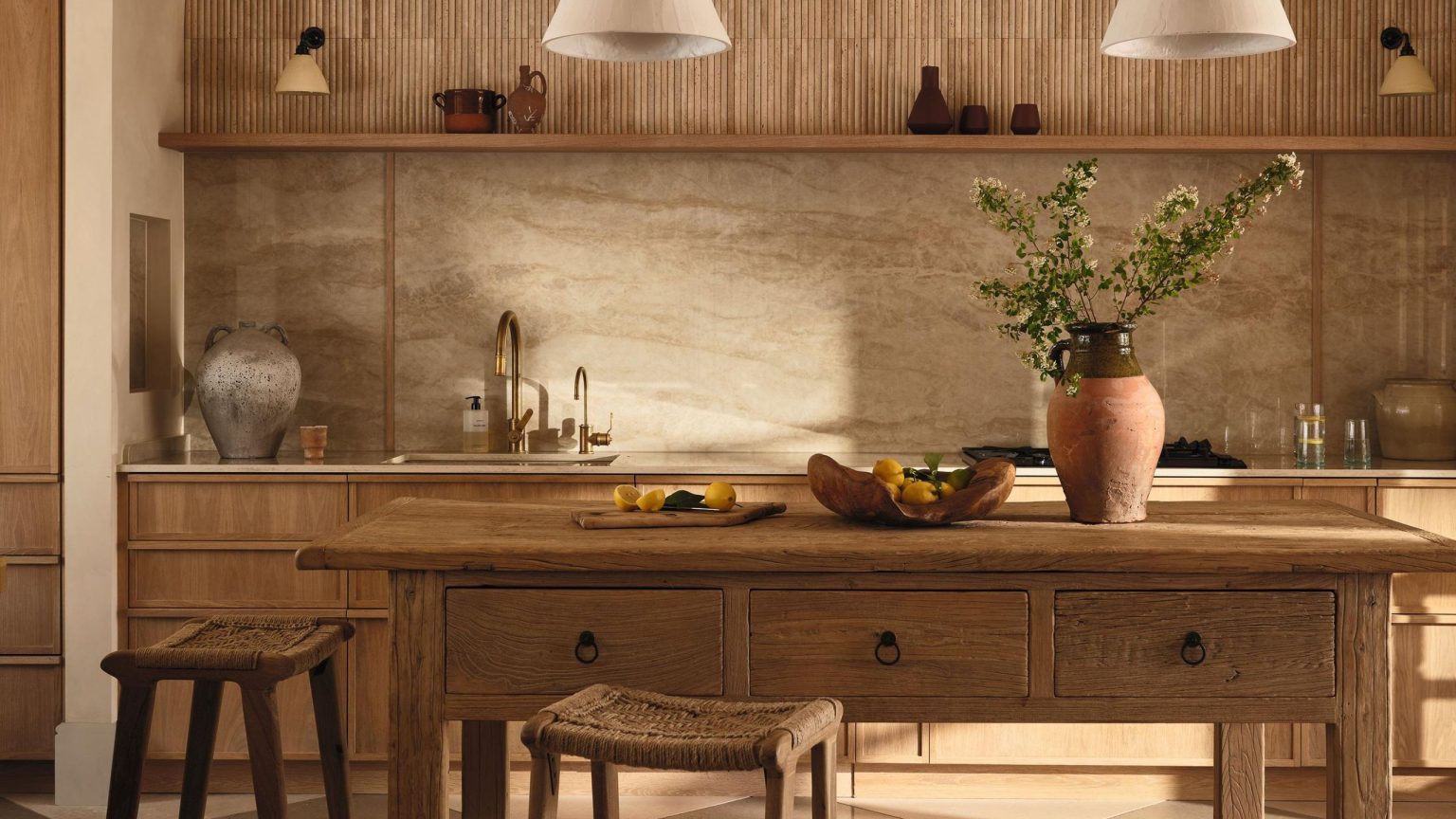 Oubliez le bleu et le blanc – Achetez plutôt la tendance de décoration « méditerranéenne raffinée » que les créateurs adoptent à la place a rustic oak kitchen with freestanding kitchen island, woven stools and plaster pendant lights