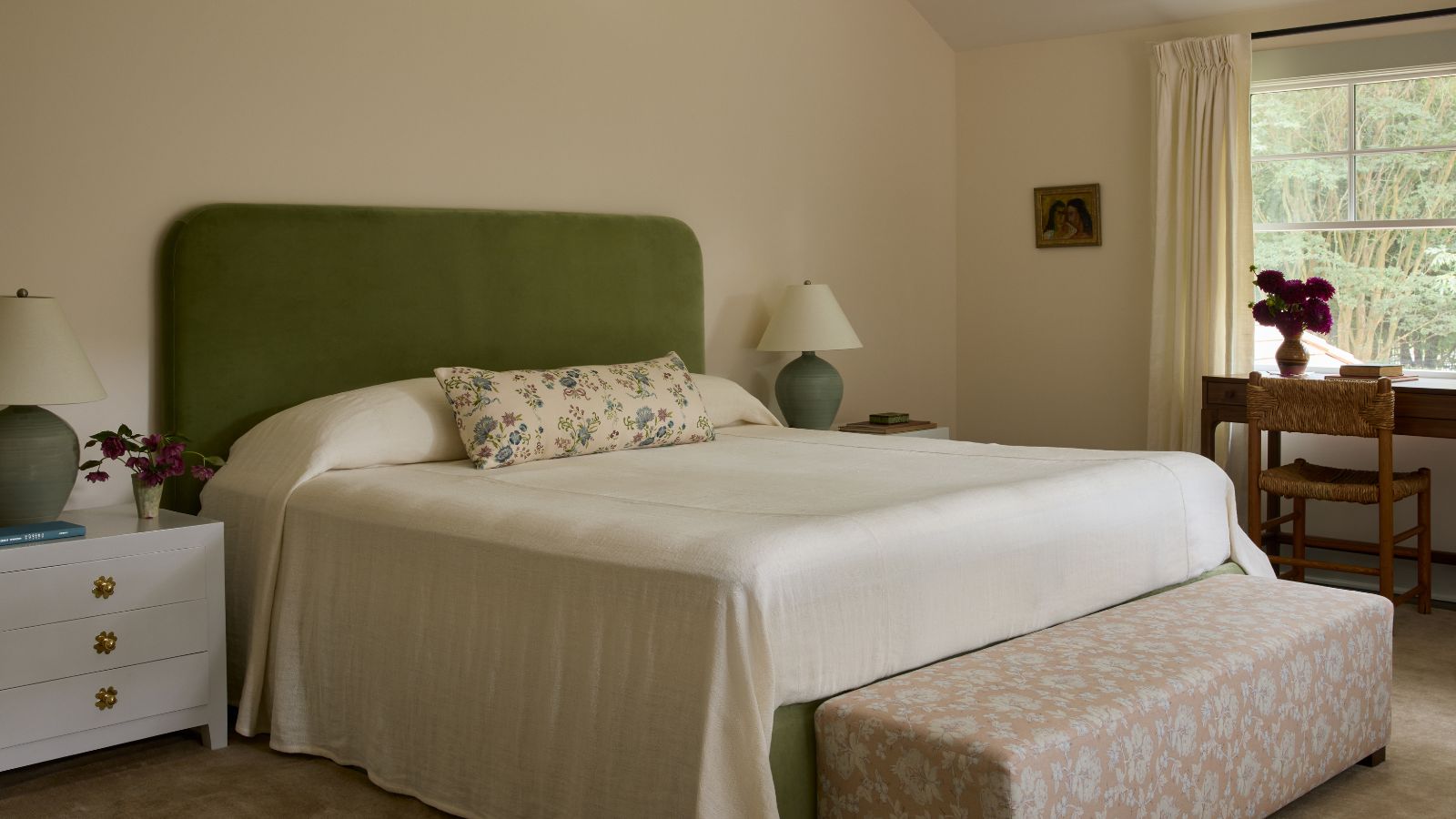 Chambre principale avec des murs blanc cassé chaleureux, une tête de lit rembourrée verte, des textiles aux accents floraux et un mobilier en bois naturel, créant une atmosphère douce et détendue.