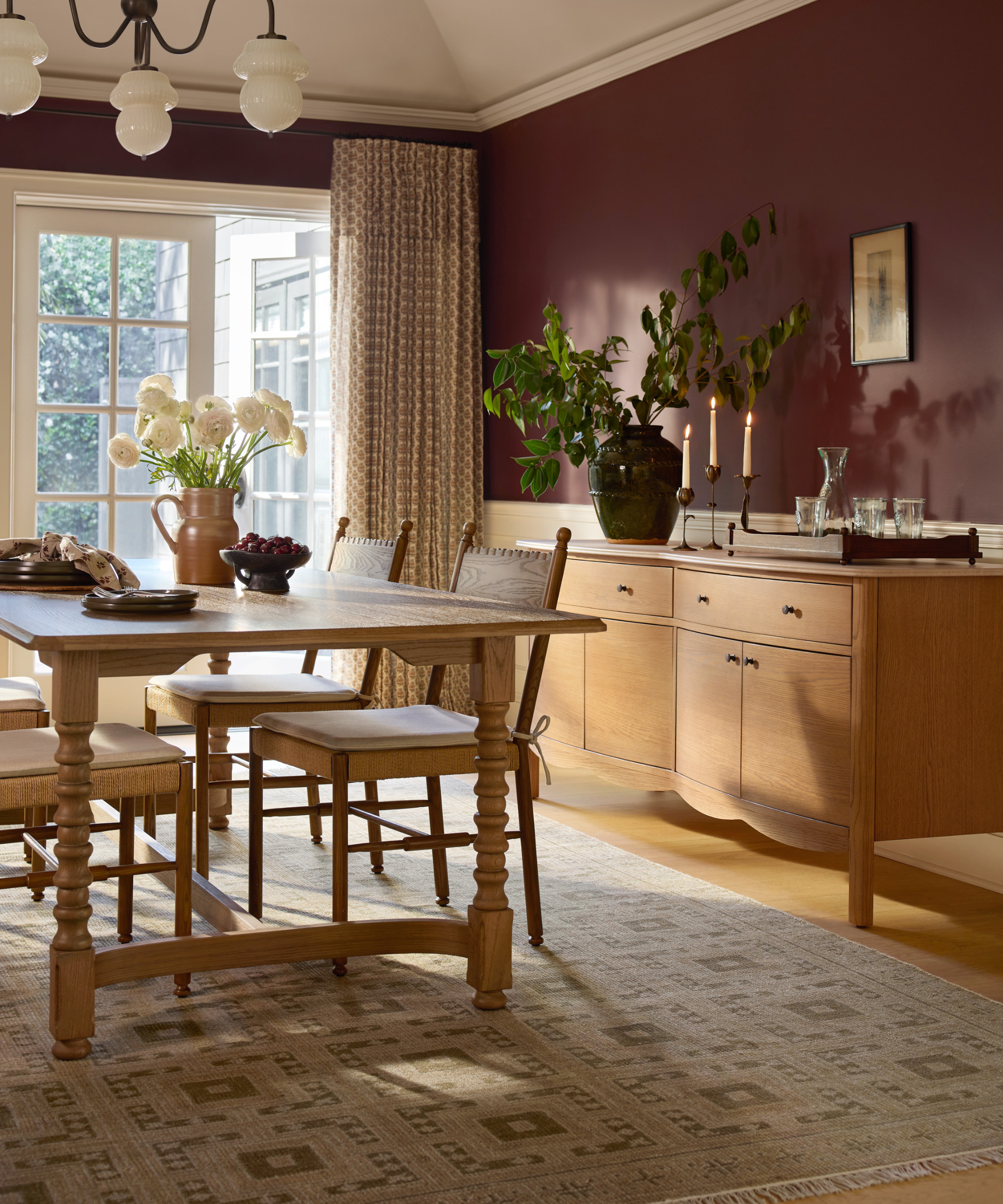 une salle à manger cosy avec une table en bois clair, des chaises, une crédence et des murs peints en marron
