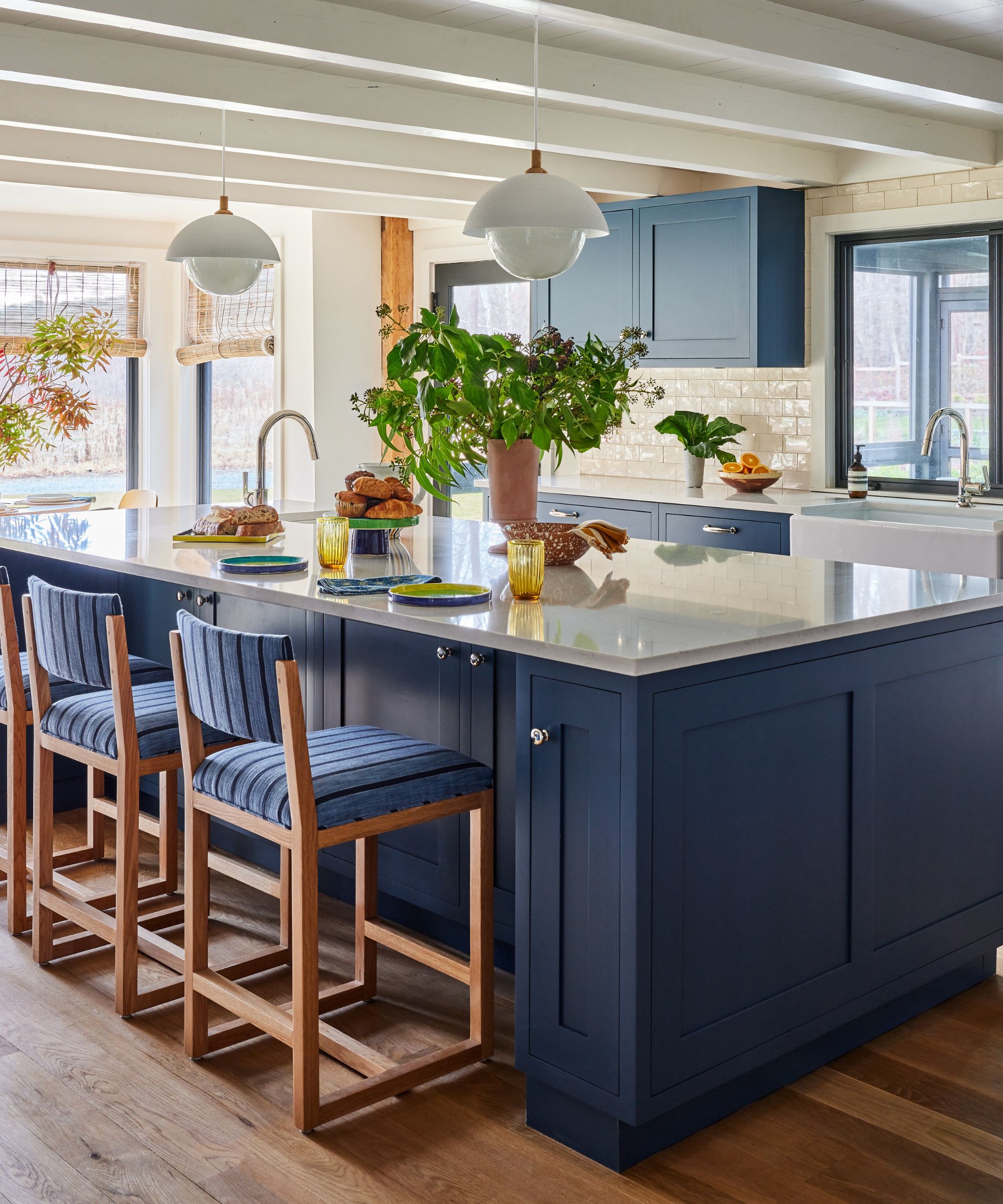 Cuisine de Sarah Lederman avec armoires Stiffkey Blue, un grand îlot avec des comptoirs blancs, un parquet en chêne et de grandes fenêtres donnant sur le paysage.